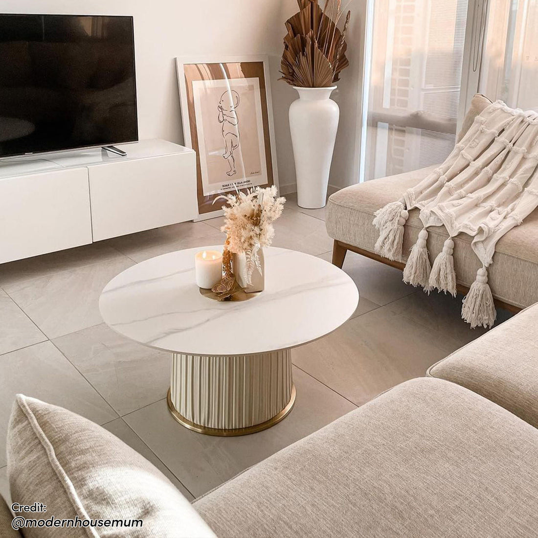 Combee 80cm Sintered Stone Coffee Table Cream White displayed with a smooth stone top and gold chromed base, enhancing a living room ambiance with a cozy white blanket and elegant glassware nearby.