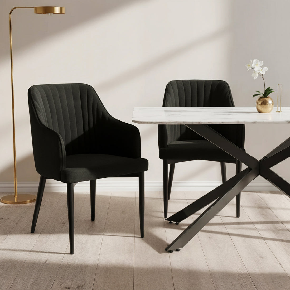 Elly Curved Velvet Dining Chairs Set of 2 in Black, featuring plush upholstery, curved high-back with armrests, and tapered legs, positioned around a marble-top table with a gold vase and orchid.