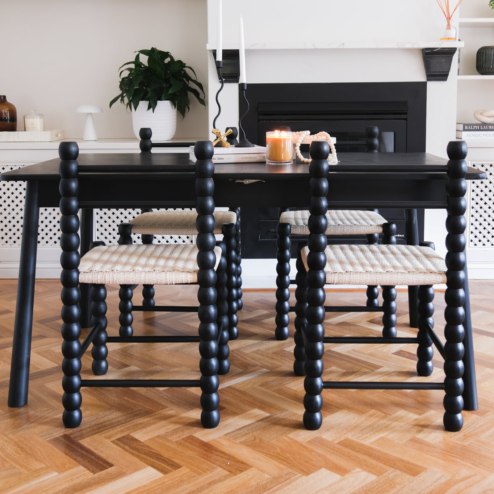 Em Solid Oak Dining Chair Set of 2 - Black, showcasing a classic bobbin-style frame and natural fibre woven seat, elegantly displayed in a cozy dining room setting with a table and chairs.