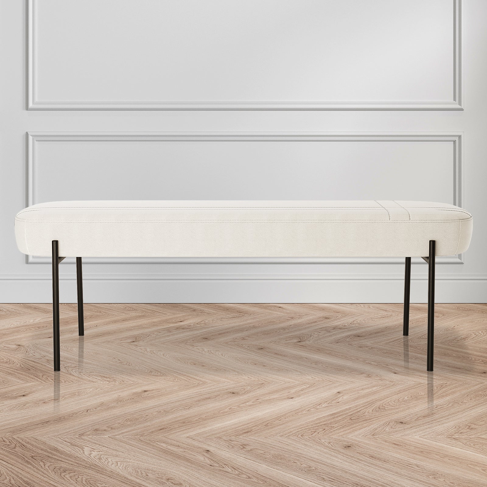 Gavin Dining Bench - Cream White features a minimalist design with a low-profile white cushion and slender black metal legs, set against a white paneled wall on a herringbone-pattern wood floor.