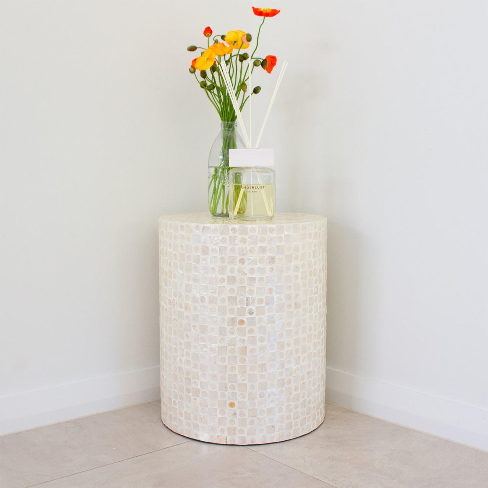 Lulu Grid Mother of Pearl Inlay Side Table in Golden, showcasing a mosaic surface, holds a vase with poppy-like flowers and a “WANDERLUST” diffuser, creating an elegant corner display.