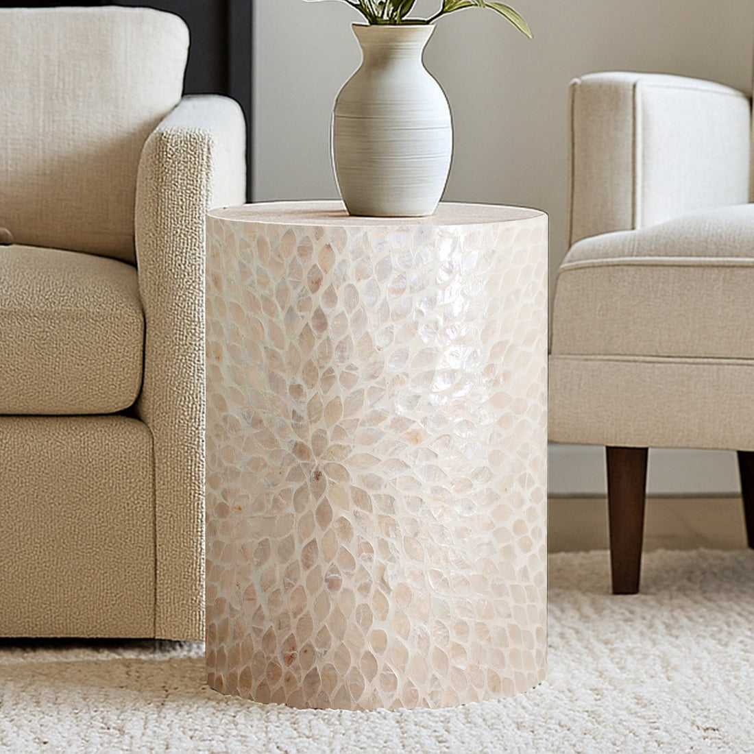 Lulu Mother of Pearl Inlay Side Table in White showcased between cream chairs, featuring a shimmering capiz mosaic surface with a matte ceramic vase and green leaves, exuding elegance and sophistication.