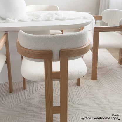 Maddi Boucle Hardwood Dining Chair in Cream White: Modern design with pale oak frame, curved back, and textured off-white boucle upholstery, set in a minimalist dining nook with matching furniture and soft decor elements.