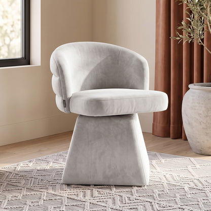 Grey swivel dining chair with a curved channeled back and chunky square pedestal base, set on a geometric rug.