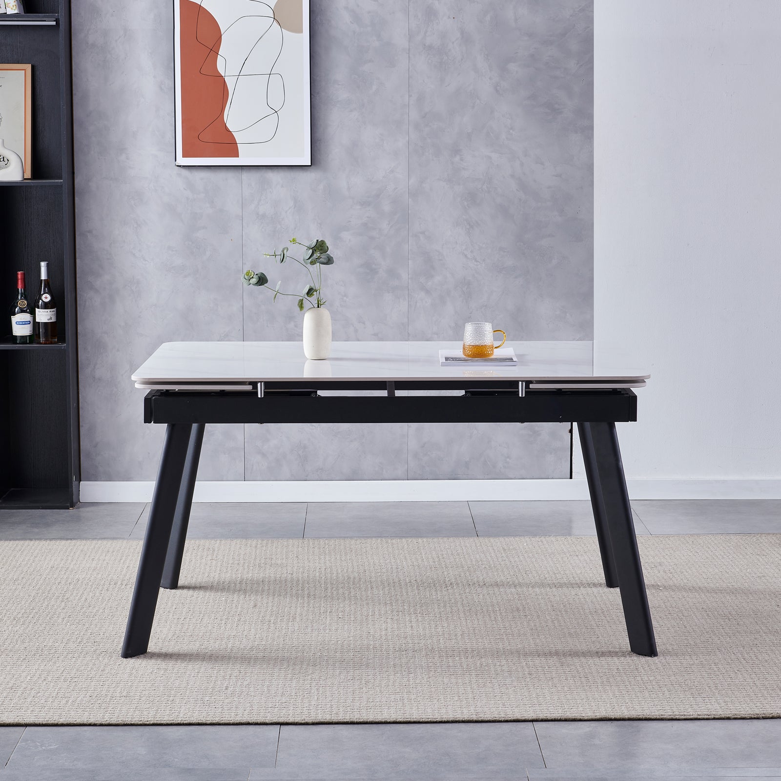Rheed 197cm Extendable Ceramic Porcelain Dining Table White features a smooth white tabletop with black legs, complemented by a ceramic vase with greenery and a glass mug on a book.