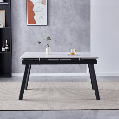 Rheed 197cm Extendable Ceramic Porcelain Dining Table White features a smooth white tabletop with black legs, complemented by a ceramic vase with greenery and a glass mug on a book.