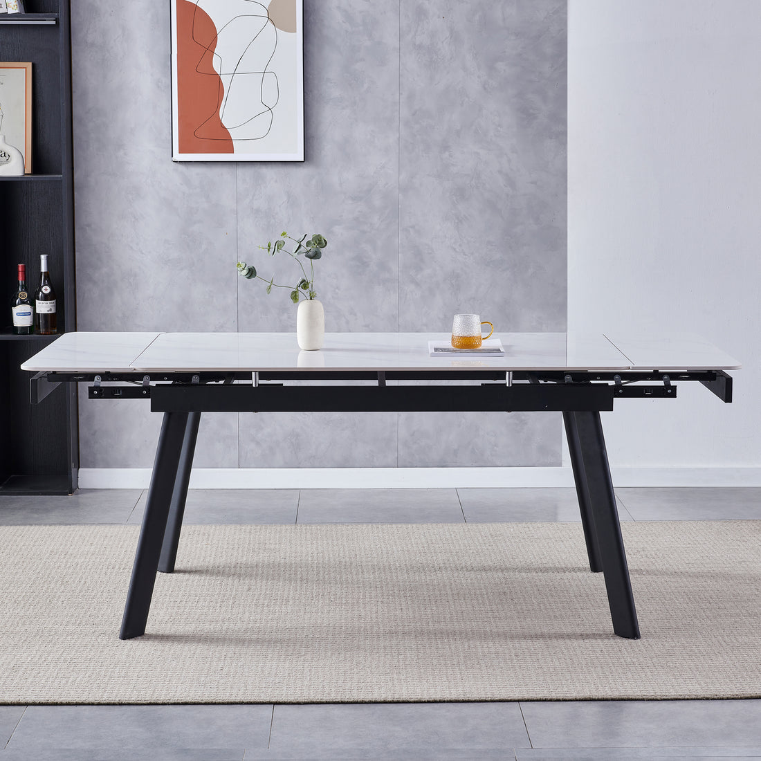 Rheed 197cm Extendable Ceramic Porcelain Dining Table White with a marble-effect top, black angled legs, and partially extended leaves, adorned with a ceramic vase and glass mug on a woven rug.