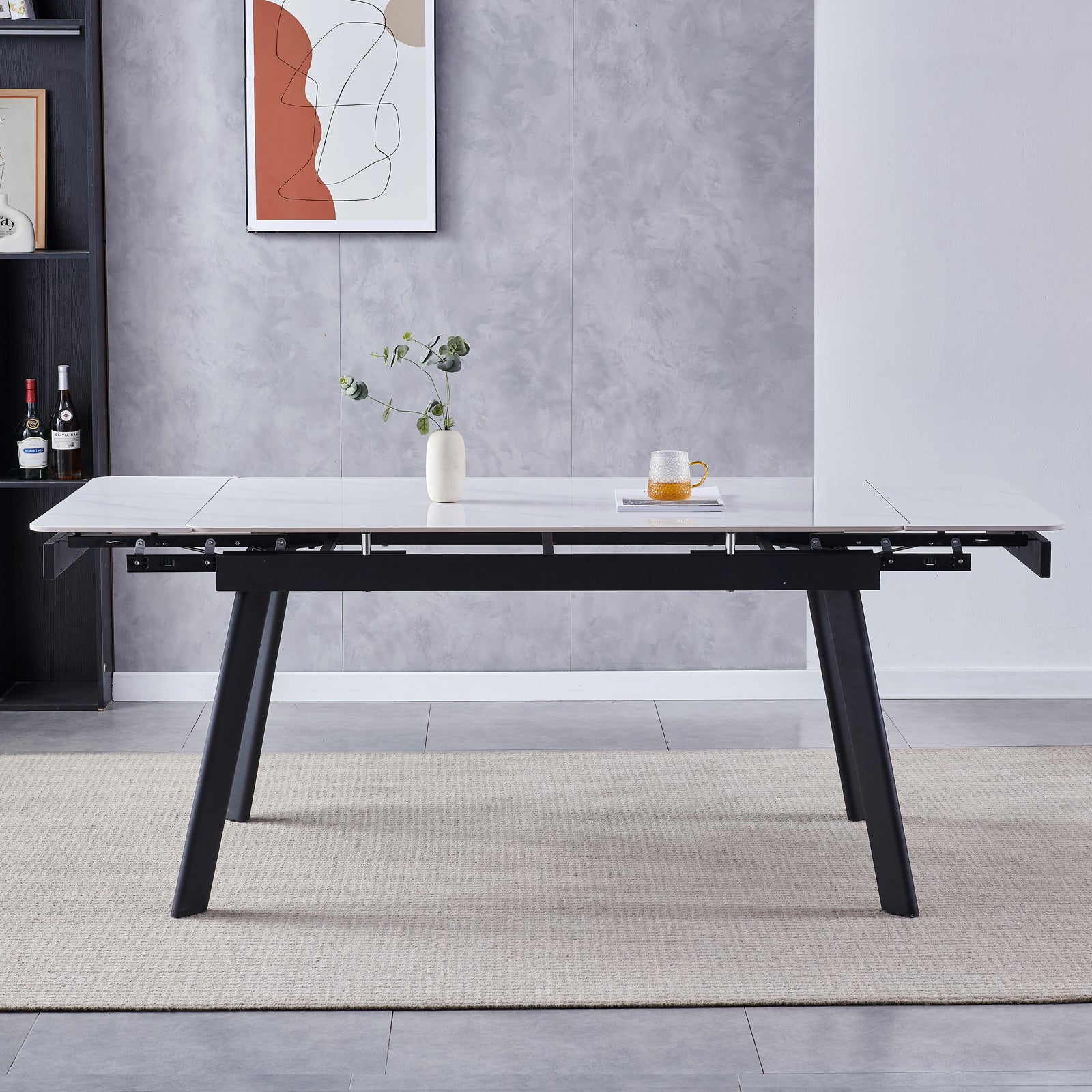 Rheed 197cm Extendable Ceramic Porcelain Dining Table White with a marble-effect top, black angled legs, and partially extended leaves, adorned with a ceramic vase and glass mug on a woven rug.