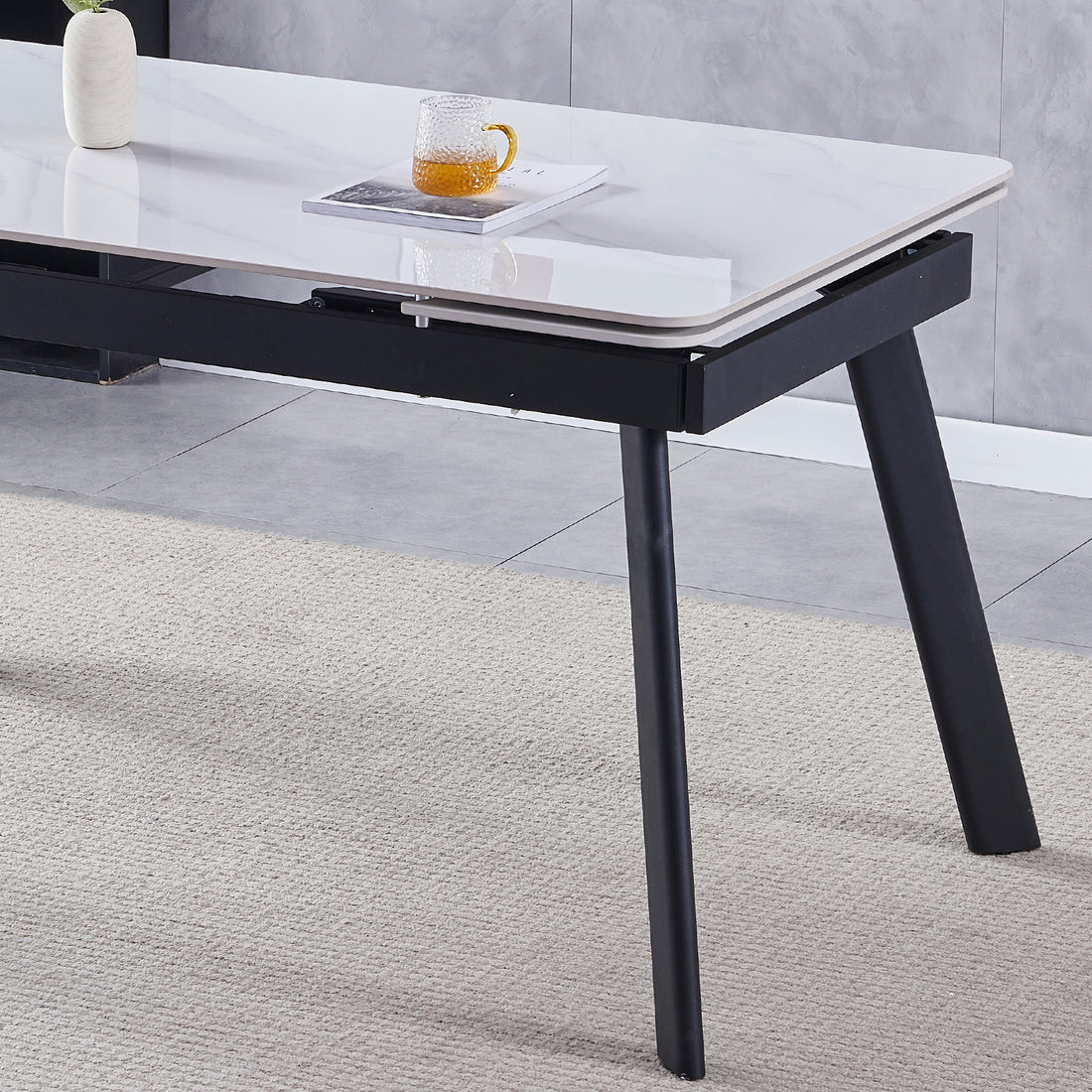 Rheed 197cm Extendable Ceramic Porcelain Dining Table White with a sleek white marble-look top and sturdy black splayed metal legs, adorned with a small vase and a glass mug on an open magazine.