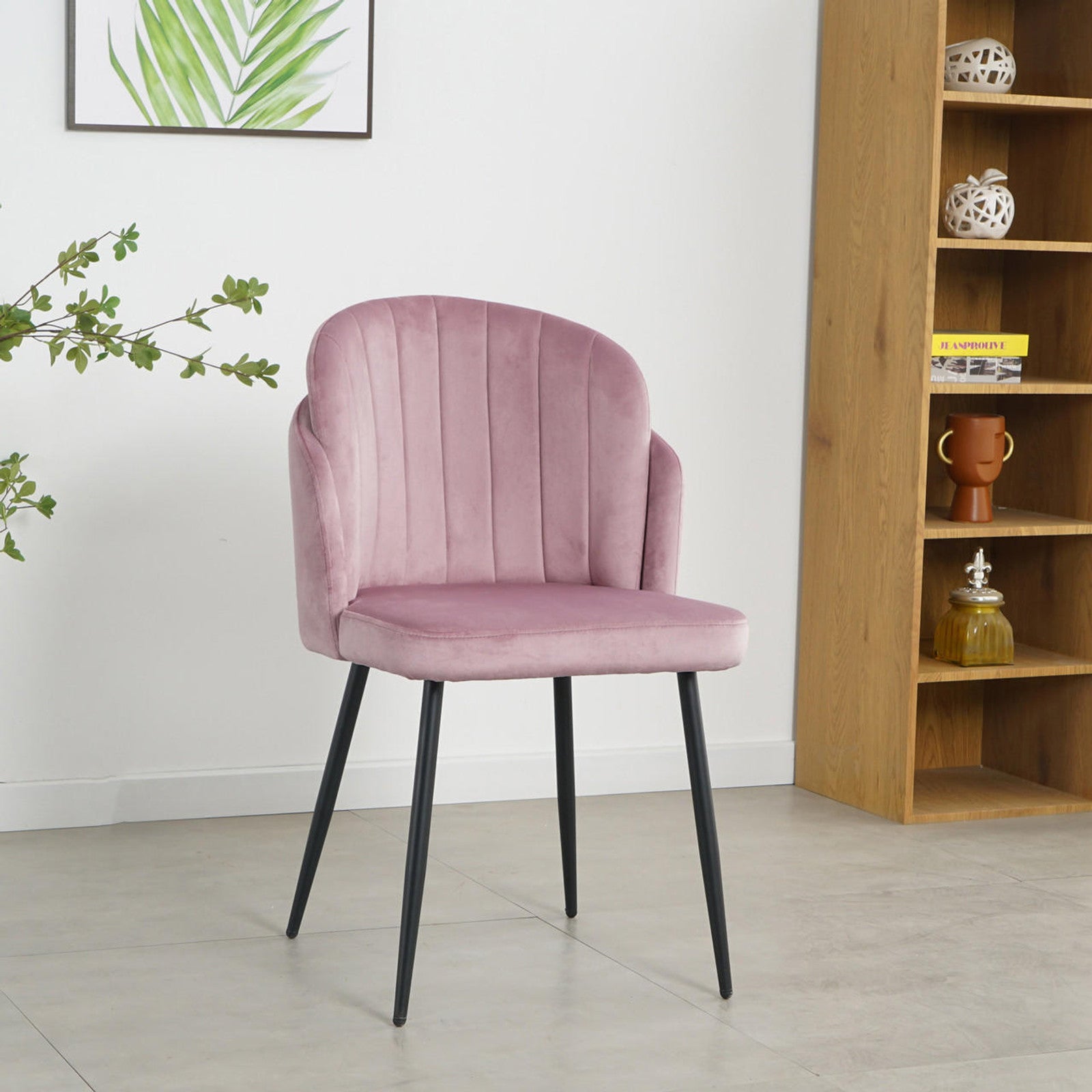 Scarlett Velvet Dining Chair Set of 2 in Mauve Pink, featuring blush-pink velvet upholstery with vertical channel stitching, black tapered metal legs, on a light gray floor, framed by a plant and shelving unit.