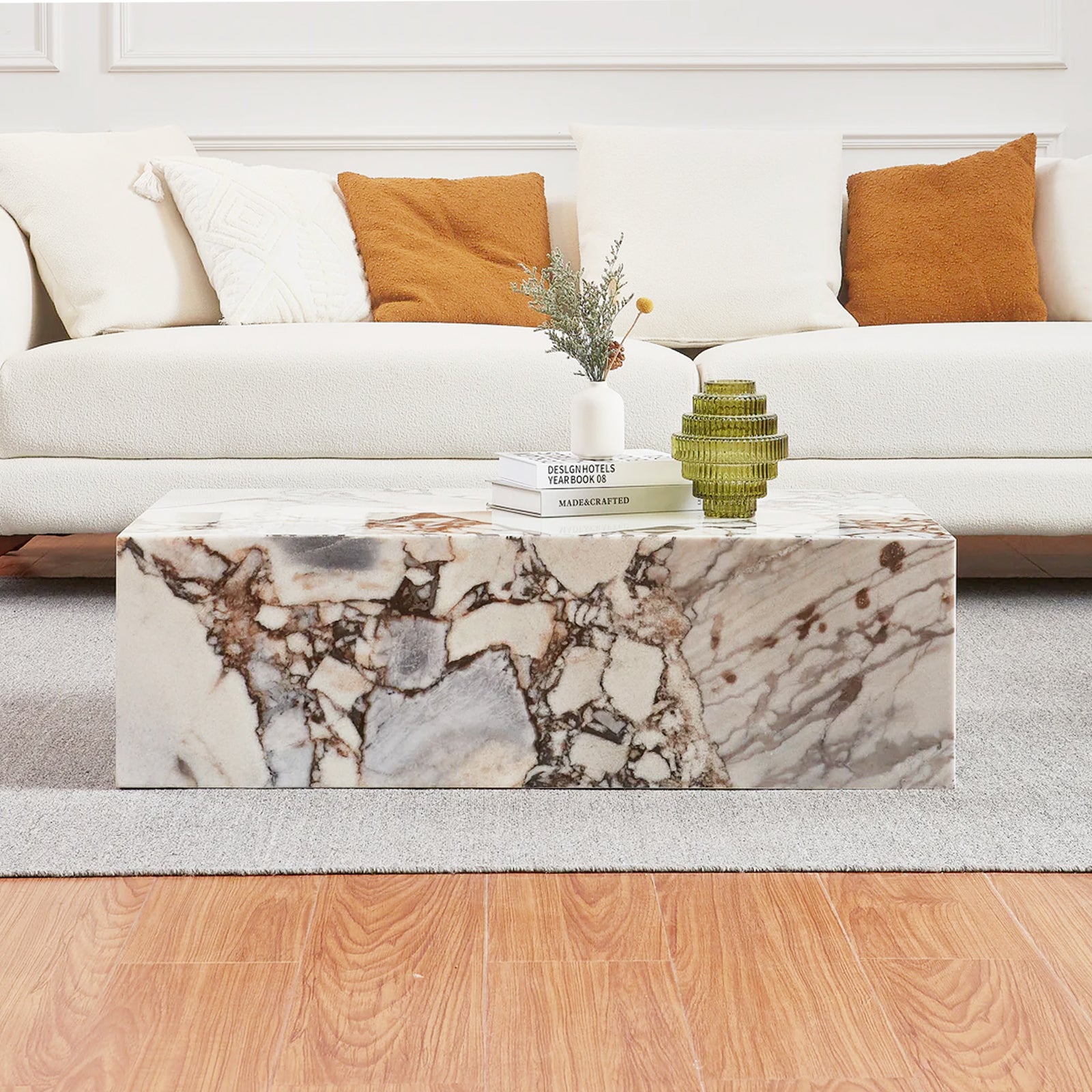 Solene 100cm Coffee Table in Real Blue Galaxy Marble on a gray rug, adorned with books, a ceramic vase with greenery, and a green decorative glass object, in front of an off-white sofa.