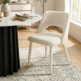 Cream upholstered chair next to round table in a bright dining room