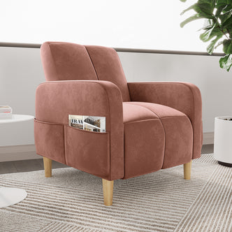 The Anica Single Seater Velvet Fabric Sofa Chair in Blush features a modern design with a built-in fabric pocket, natural-wood legs, and wide armrests, set on a striped area rug.