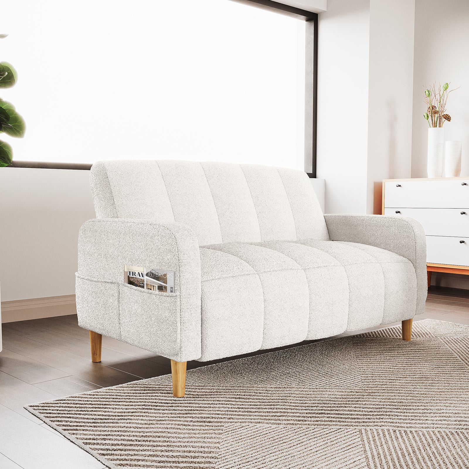 Anica 2 Seater Boucle Fabric Sofa Bed in Cream White, featuring a light boucle fabric, short wooden legs, built-in side pocket with magazines, set against a bright window in a minimalist living-room corner.