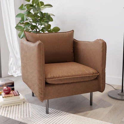 Cassian PU Leather Armchair in Chocolate Brown, featuring warm upholstery, broad padded armrests, slim metal legs, surrounded by a houseplant, books, and an apple, on a light-wood floor.