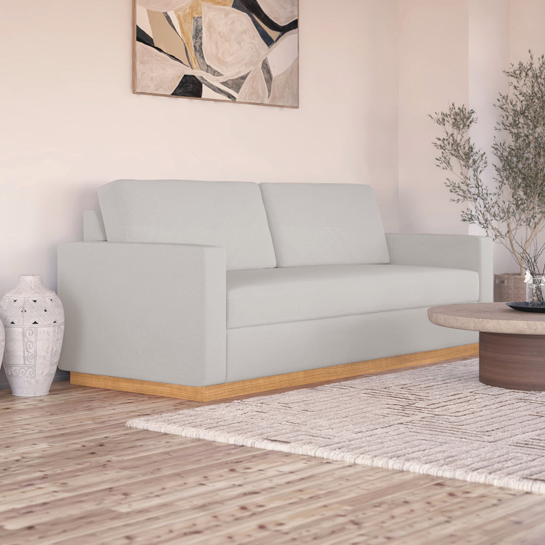Celeste 3 Seater Hardwood Fabric Sofa with removable cushions and wood accent legs, showcasing its sturdy frame and sleek design in an interior setting with a painting and a studio couch nearby.