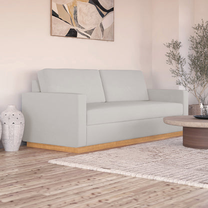 Celeste 3 Seater Hardwood Fabric Sofa with removable cushions and wood accent legs, showcasing its sturdy frame and sleek design in an interior setting with a painting and a studio couch nearby.