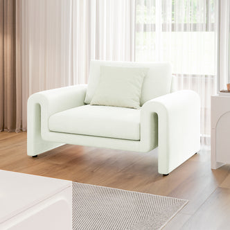 Celyn Curved Velvet Single Sofa Accent Chair in Cream with soft, rounded design, paired with a matching pillow, sits on light-toned hardwood flooring with sheer curtains diffusing natural light behind.