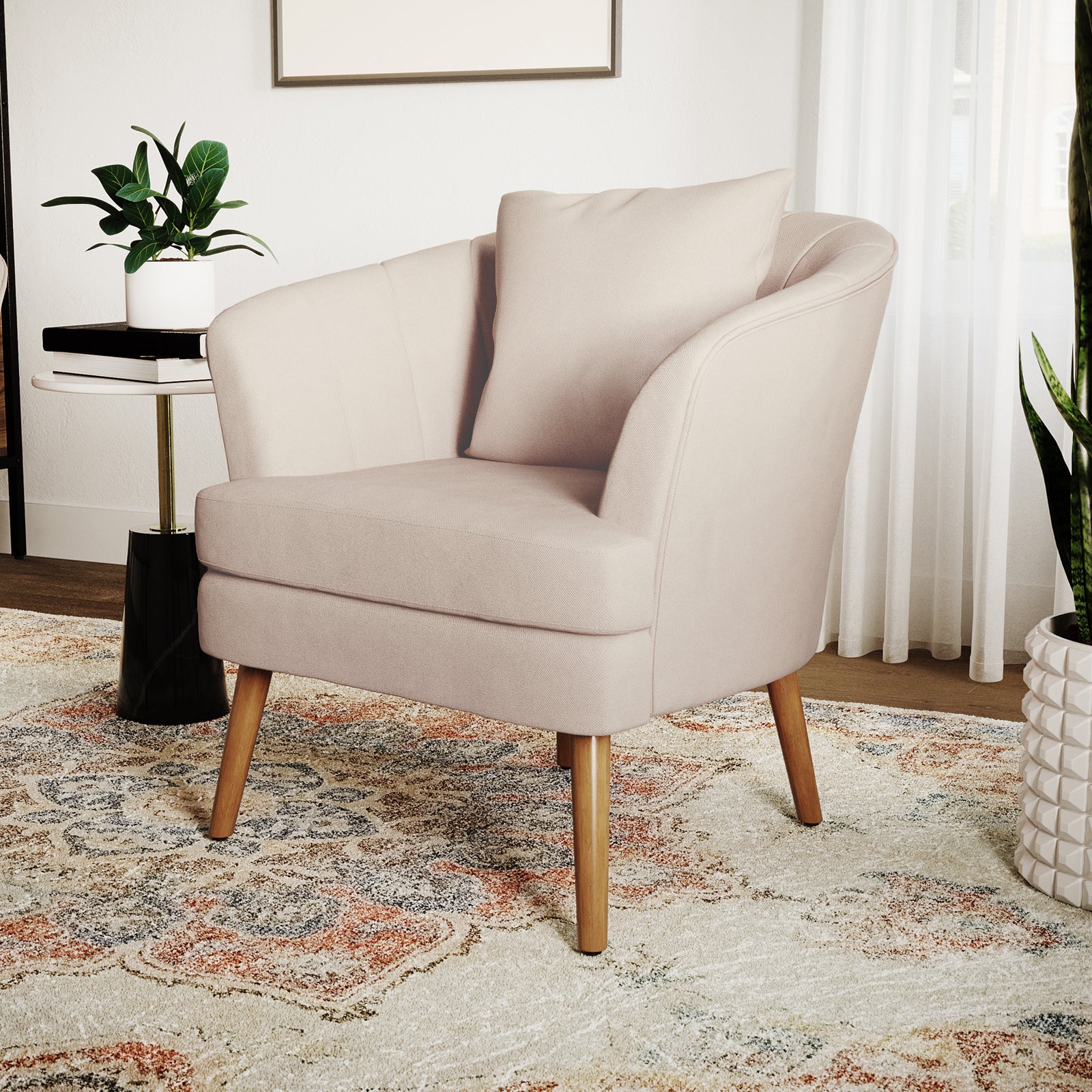 Dalya Linen Accent Chair with Cushion Cream White, featuring blush-pink upholstery, softly curved design, slender wooden legs, and accompanied by a side table with books and a plant, against a minimalist backdrop.