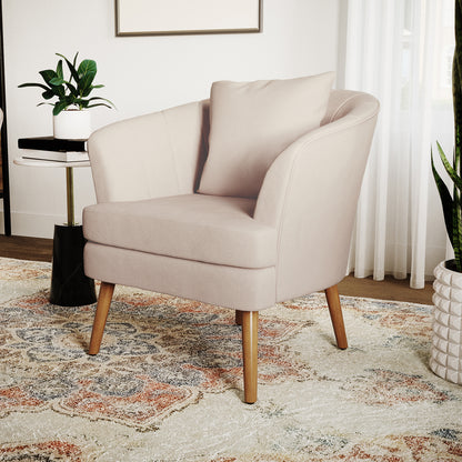 Dalya Linen Accent Chair with Cushion Cream White, featuring blush-pink upholstery, softly curved design, slender wooden legs, and accompanied by a side table with books and a plant, against a minimalist backdrop.