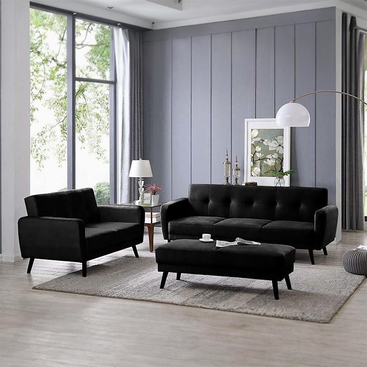 Esben Velvet Fabric Ottoman in Black serves as a coffee table in a modern living room with a matching black sofa set, complemented by Scandinavian-style wooden legs and tufted upholstery.