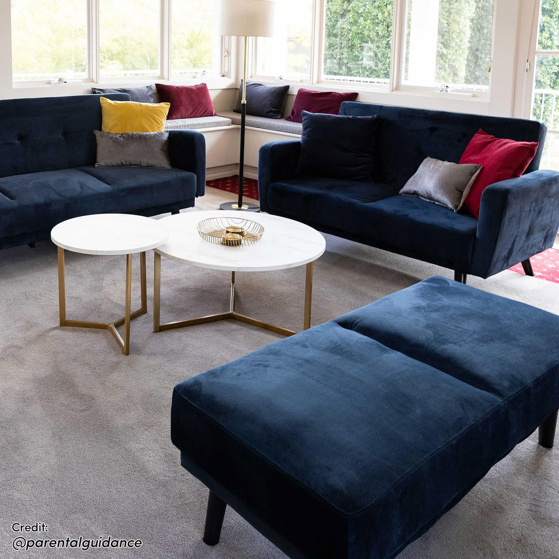 Esben 2-Seater Velvet Sofa Bed in Navy Blue, featuring sleek design, plush upholstery, and tufted seating, positioned centrally in a bright living room with modern decor elements like nesting tables and assorted pillows.