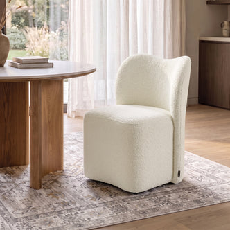 Cream bouclé upholstered swivel dining chair with a high backrest, set at a wooden table in a dining room.   