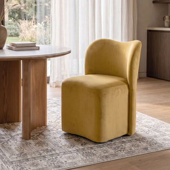 Alt-text: Mustard gold upholstered swivel dining chair with a high backrest, set at a wooden table in a dining room.   