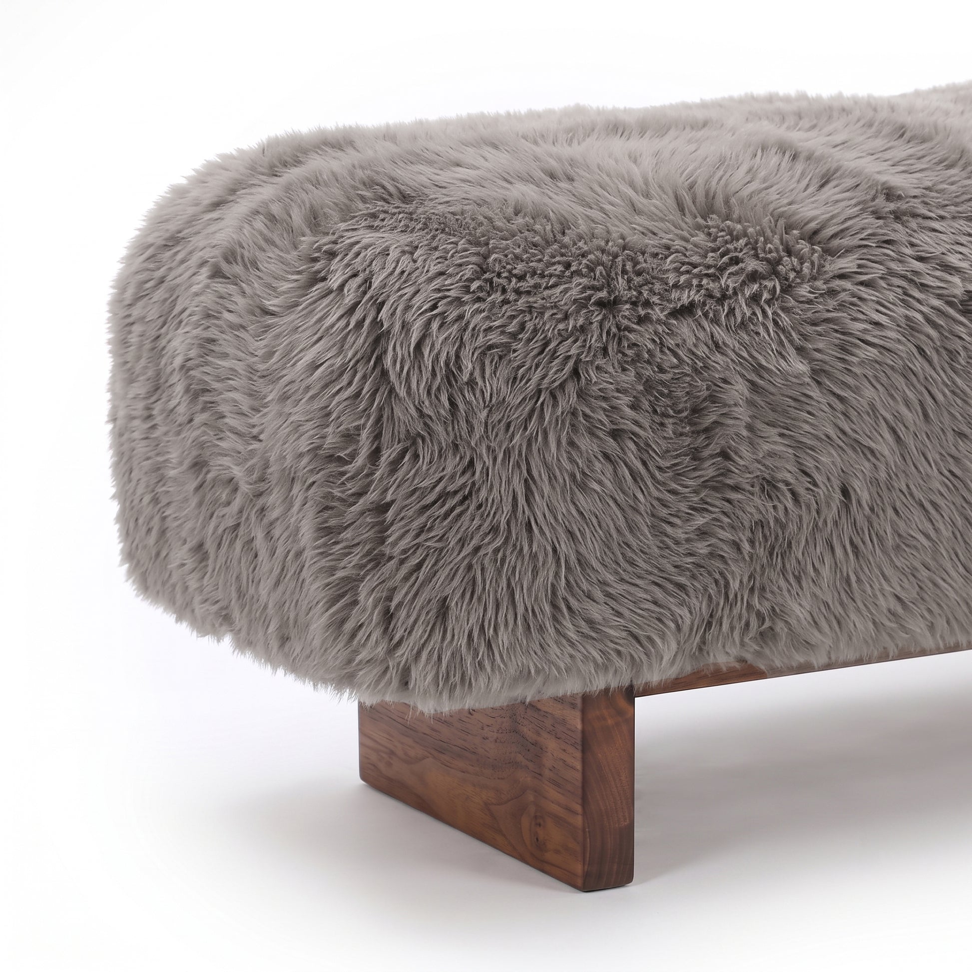 A close-up detail view of the taupe faux-fur or sheepskin upholstered bench, highlighting the plush, long-pile texture of the fabric meeting the clean edge of the dark wooden block leg against a plain white background