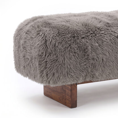 A close-up detail view of the taupe faux-fur or sheepskin upholstered bench, highlighting the plush, long-pile texture of the fabric meeting the clean edge of the dark wooden block leg against a plain white background