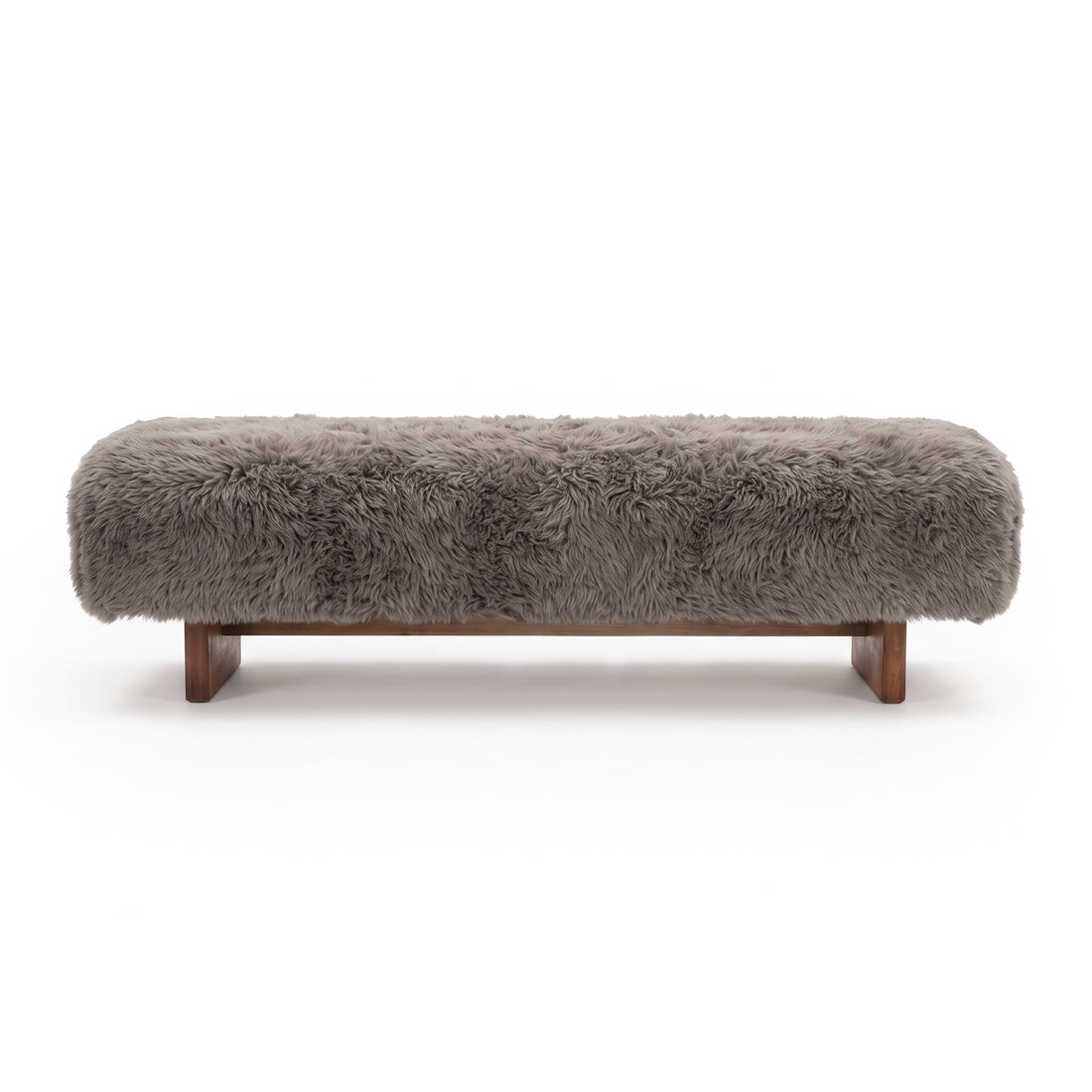 A straight-on view of the taupe faux-fur or sheepskin upholstered bench, showcasing its long-pile plush texture and low dark wooden block legs against a clean white background.