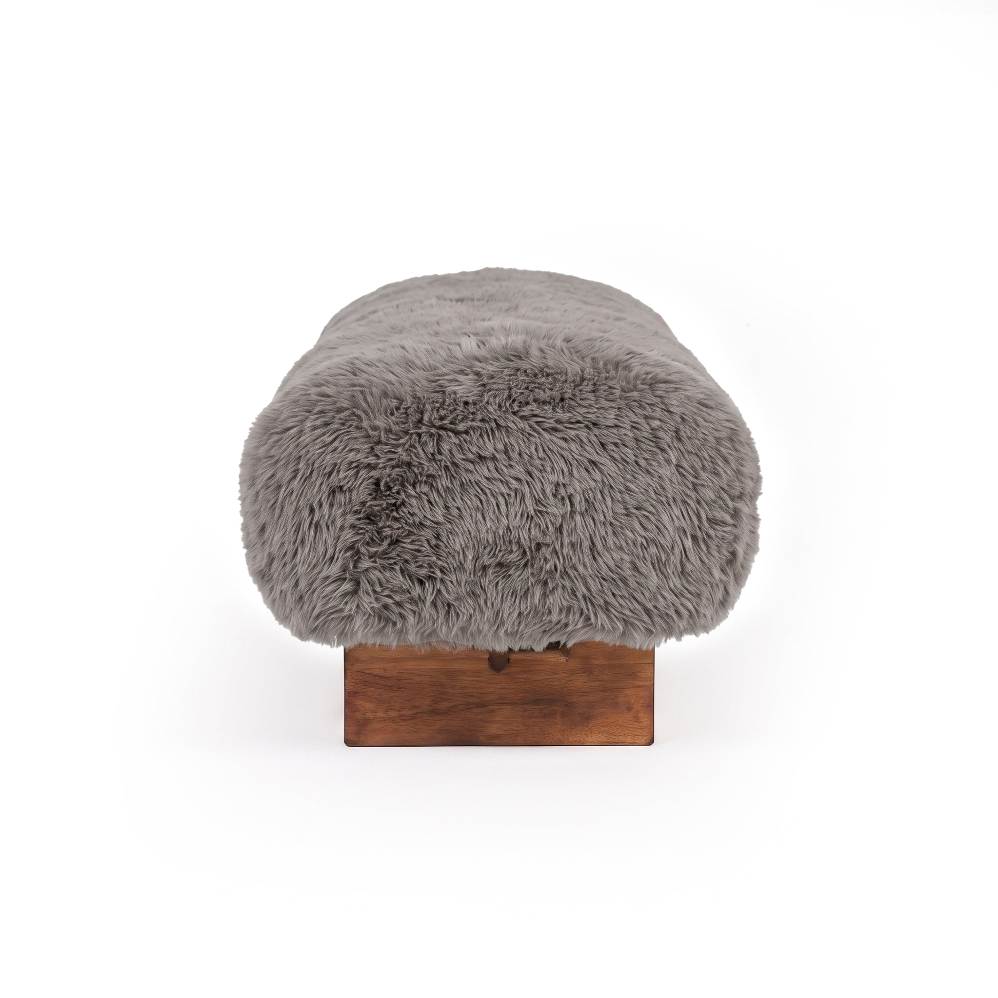 A profile, end-on view of the taupe faux-fur or sheepskin upholstered bench, showcasing its rounded edge profile and low dark wooden block leg against a clean white background.