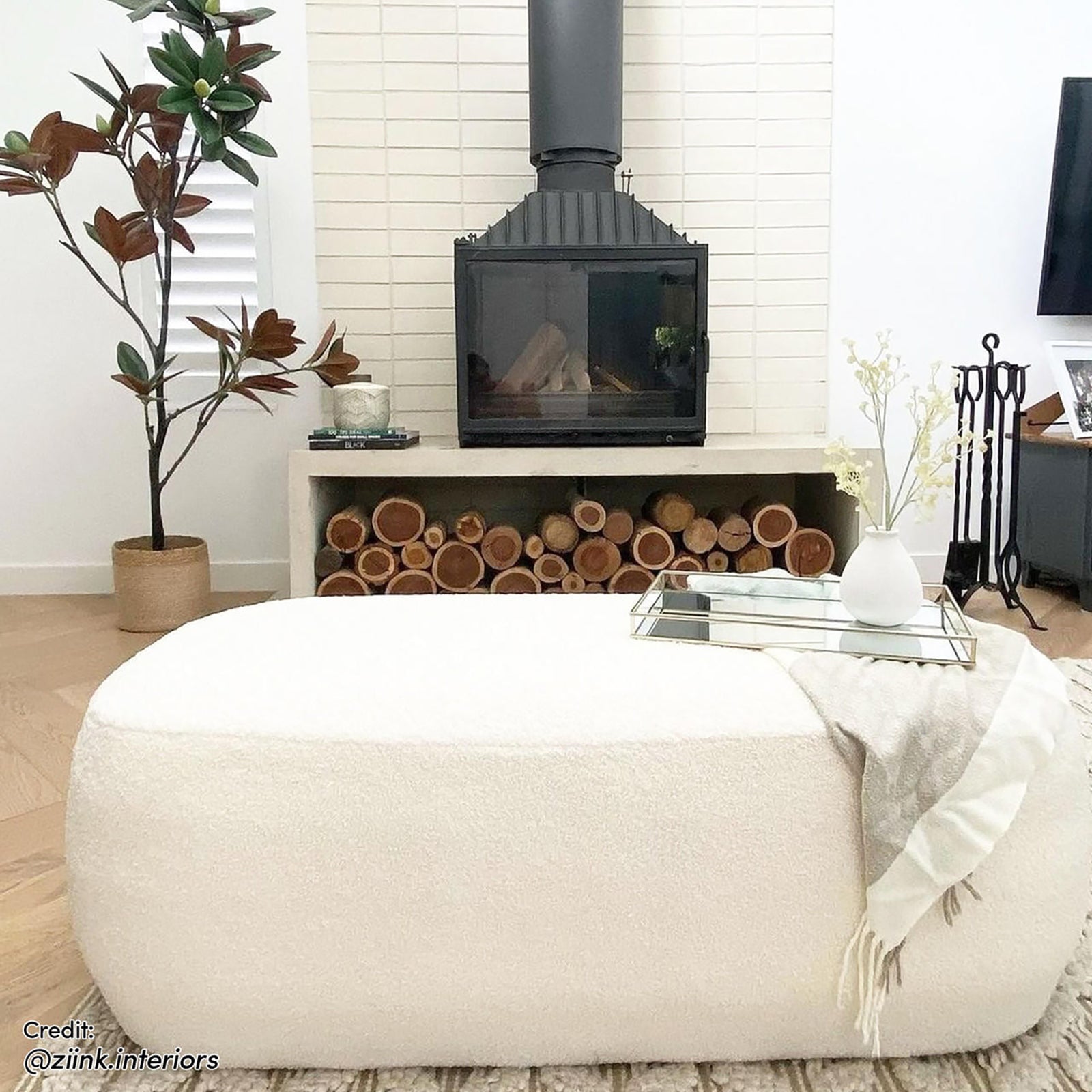 Jamie 110cm Bouclé Ottoman in Cream White is a large, rounded ottoman with a textured surface, placed in a minimalist living room, topped with a mirrored tray and small vase.