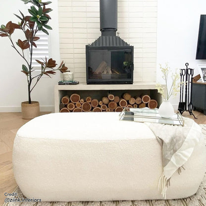 Jamie 110cm Bouclé Ottoman in Cream White is a large, rounded ottoman with a textured surface, placed in a minimalist living room, topped with a mirrored tray and small vase.
