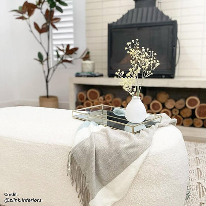 Jamie 110cm Bouclé Ottoman in Cream White, upholstered with a cozy texture. Features a soft two-tone throw and a mirrored tray with a ceramic vase, set in a modern living-room scene.