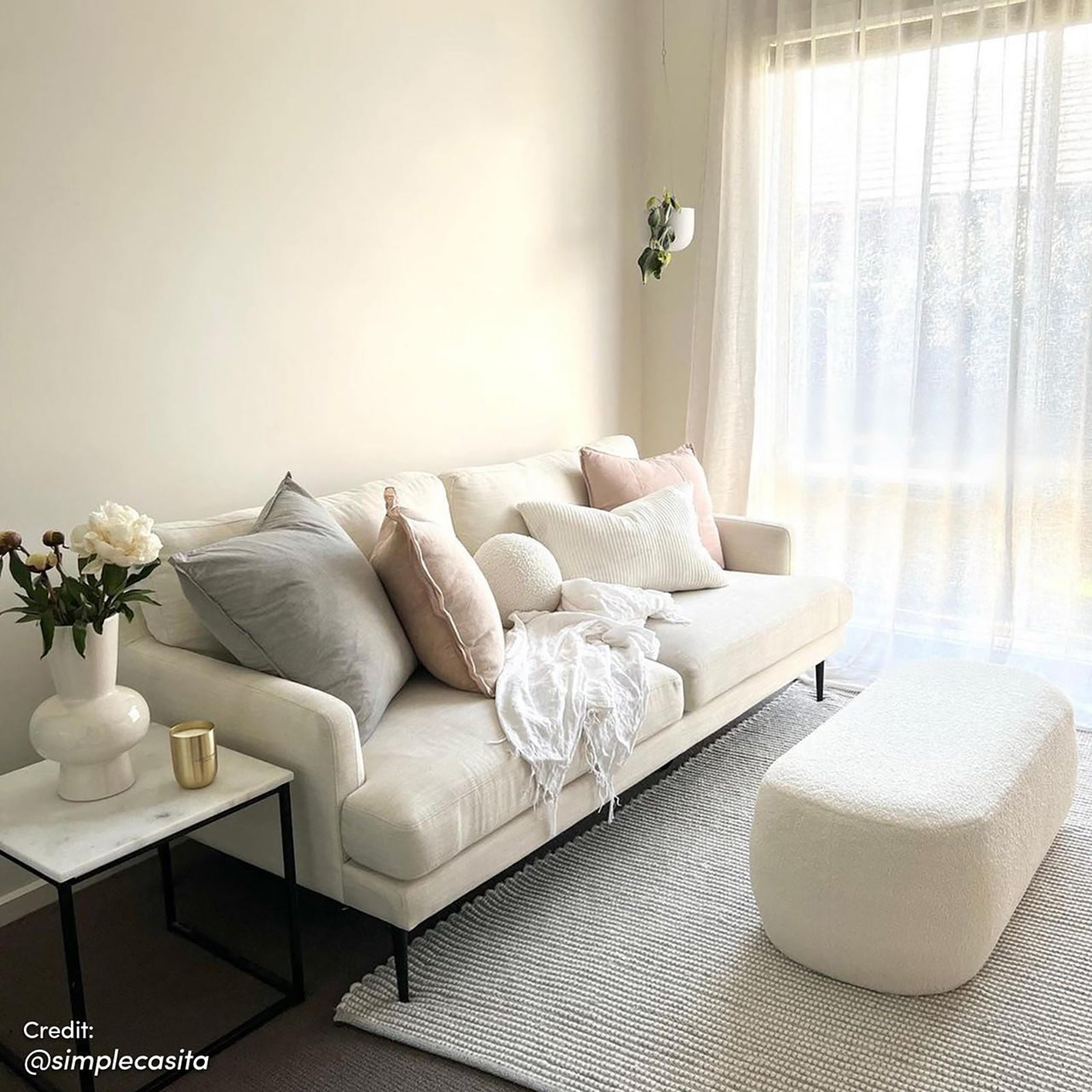 Jamie 110cm Bouclé Ottoman in Cream White, featuring a rounded shape and rich texture. Positioned on a light-gray rug, it complements a cream-colored sofa and adds elegance to the living room setting.