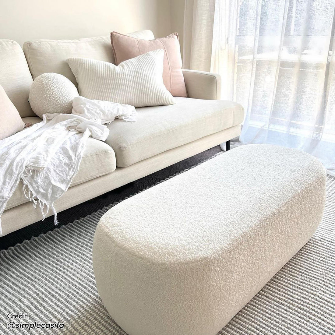 Jamie 110cm Bouclé Fabric Ottoman in Cream White, pill-shaped and upholstered in ivory bouclé, sits in a bright living room, serving as a stylish, spacious centerpiece for relaxation.
