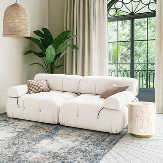 Keila 2 Seater Sofa & Side Table Package in Cream Velvet, featuring a modular sofa with tufted design, checkerboard and solid cushions, paired with a cream mother-of-pearl side table, and leafy plant backdrop.