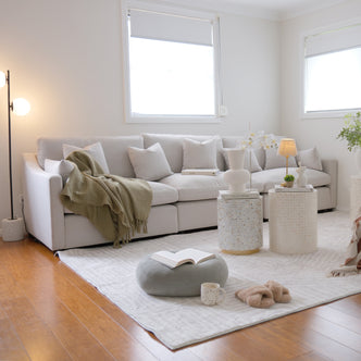 Millie 4-Seater Fabric Modular Sofa - Warm Light Grey, shown with a white pillow and blanket on a couch, highlighting its plush seating and modular design for comfort and adaptability in living spaces.