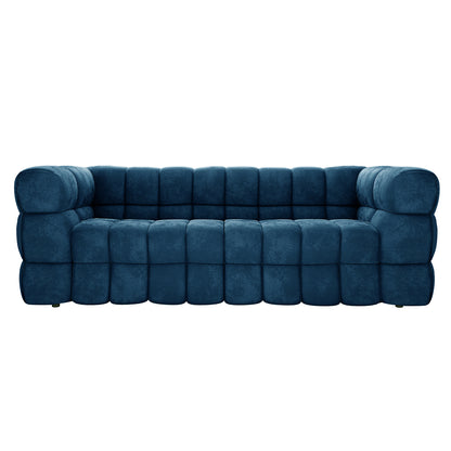 The Norah 3 Seater Velvet Sofa in Blue features a plush, deep-tufted design with rounded, grid-patterned cushioning, offering a modern and elegant look for contemporary living rooms.