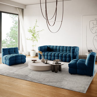 Norah 5 Seater Velvet Fabric Sofa Set in Blue, featuring a tufted three-seat sofa and two armless chairs on a light-gray rug, complemented by modern coffee tables and a sculptural pendant light.