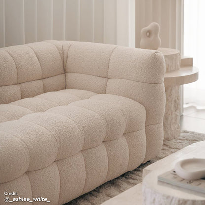 Norah 5 Seater Boucle Fabric Sofa Set in Cream White features cream-colored tufted upholstery and armless chairs, accentuated by a minimalist living room setting with sculptural elements and neutral tones.