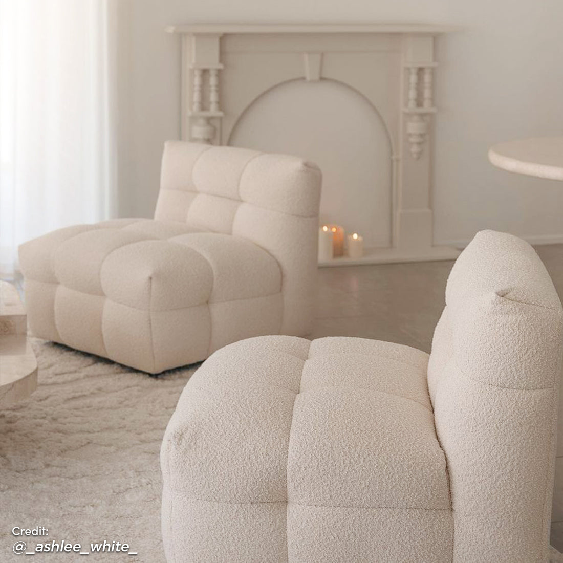 Norah 5 Seater Boucle Fabric Sofa Set in Cream White features two armless lounge chairs with tufted boucle upholstery, placed on a textured rug in front of a decorative fireplace with lit pillar candles.