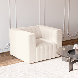 Parisa 1 Seater Tufted Boucle Single Sofa in Cream White, cube-shaped with vertical channeling, rests on a textured rug, near a glass-top table with black legs and decorative items.