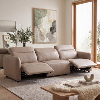 Beige sectional reclining sofa in a living room with rug, lamp, plant, and natural light