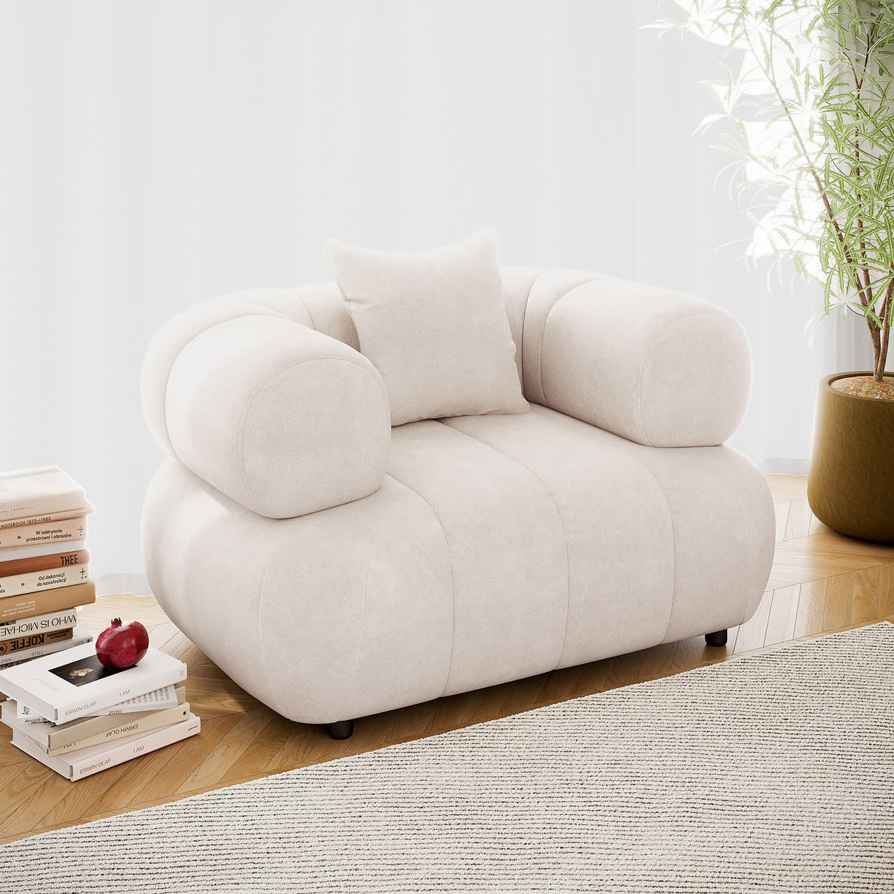Samira Single Seater Velvet Sofa in Cream features an oversized design with chunky, tubular arms and a matching throw pillow, set on a herringbone-patterned wood floor with books nearby.