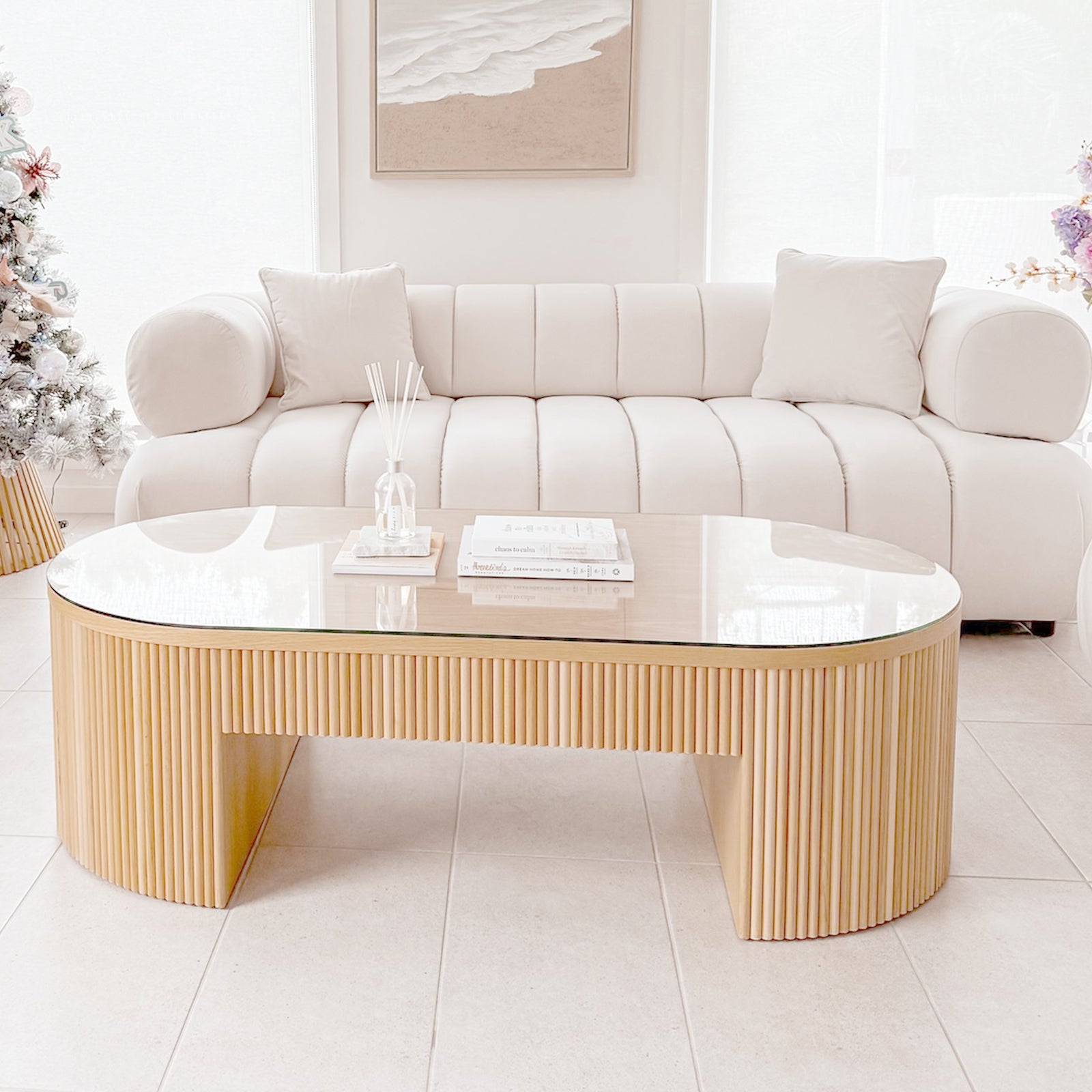 Samira 6 Seater Velvet Sofa Set in Cream, featuring rounded arms and plush cushions, sits in an elegantly styled living room corner with a minimalist coffee table and beach-inspired wall art.