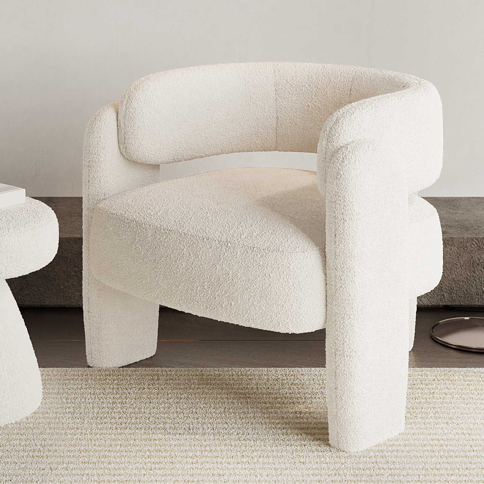 Seto Bouclé Curved Occasional Accent Chair in eggshell white, featuring a rounded backrest and arms, thick cushioning, and three chunky legs on a light-toned rug with a matching side table partially visible.