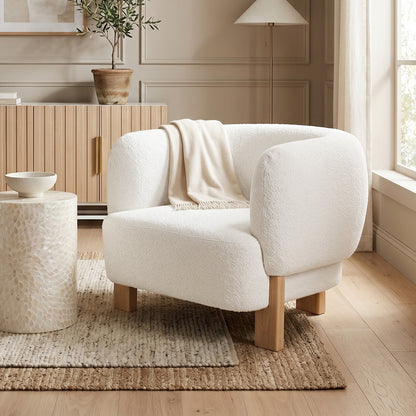Sornel Boucle Upholstered Accent Chair in Cream White, featuring a curved design with off-white bouclé fabric, light-wood legs, and a cream throw, set in a minimalist living-room corner.