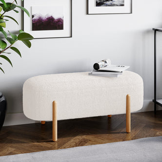 Suellen 108cm Boucle Fabric Ottoman Bench in Cream White, showcasing boucle texture and mid-century wooden legs, placed in an elegant indoor setting with a vase and stylish furniture.